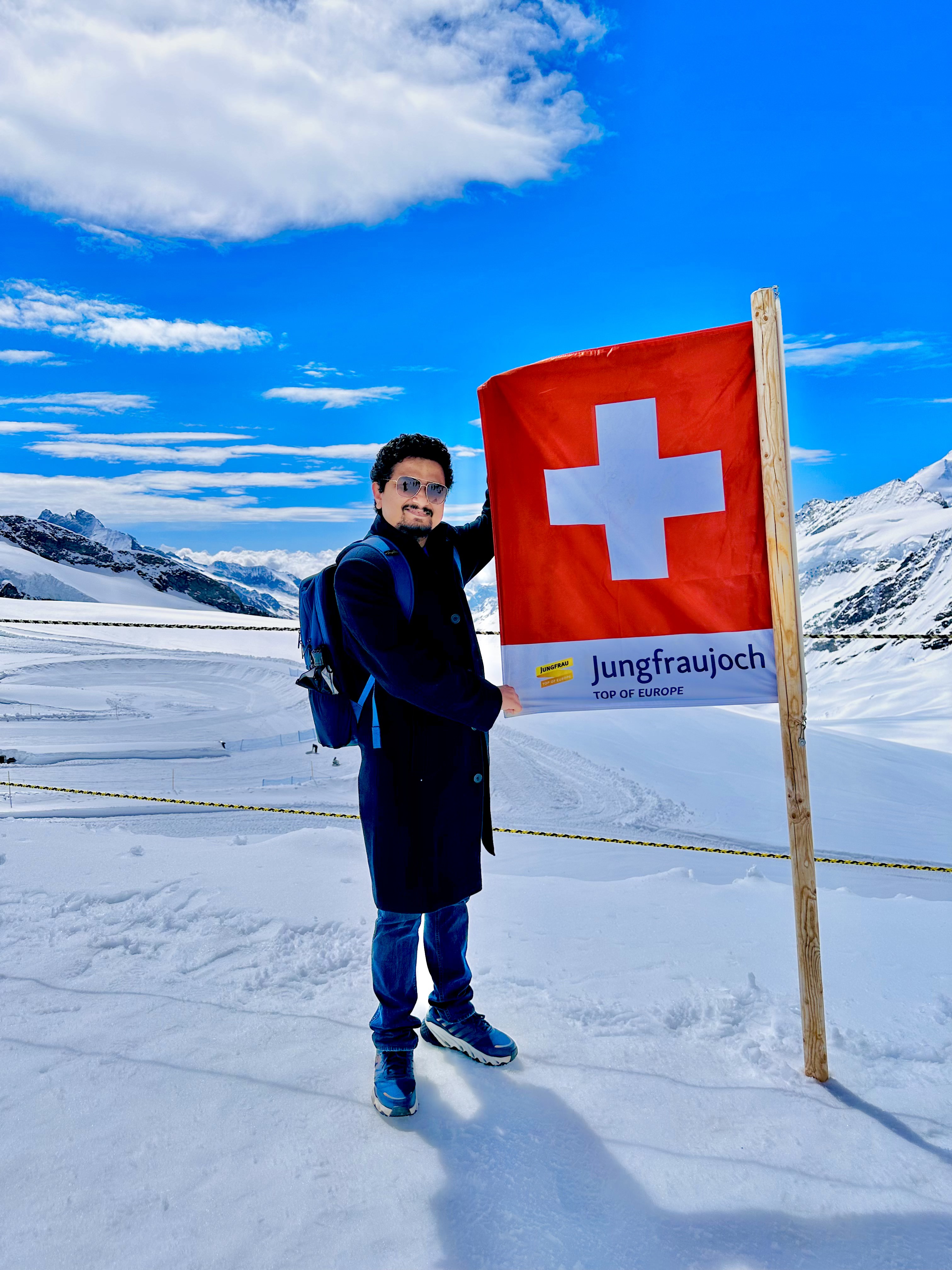 Abhishek at Jungfraujoch, Switzerland, holding a Swiss flag in the snow
